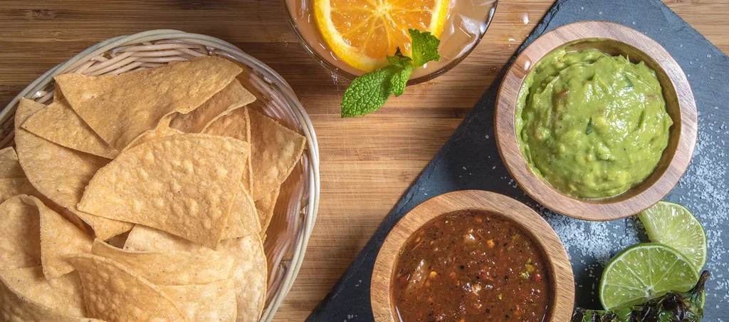 Top-down view: chips, guacamole, salsa, drink, lime, pepper on platter.