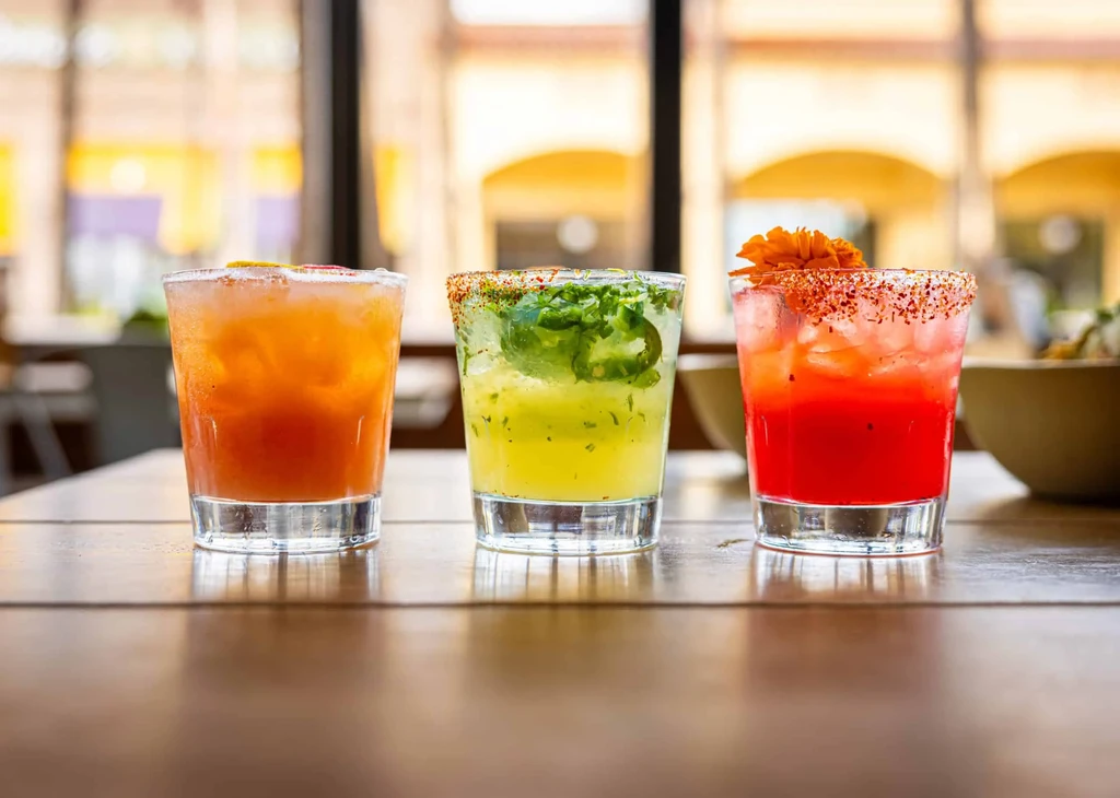 Three vibrant cocktails with ice and varied garnishes on a table.