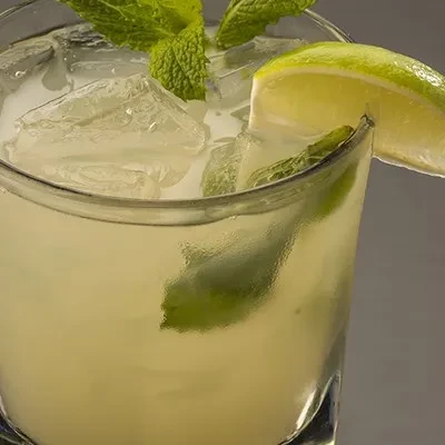 Cold lime drink with ice, mint, and lime wedge in clear glass.