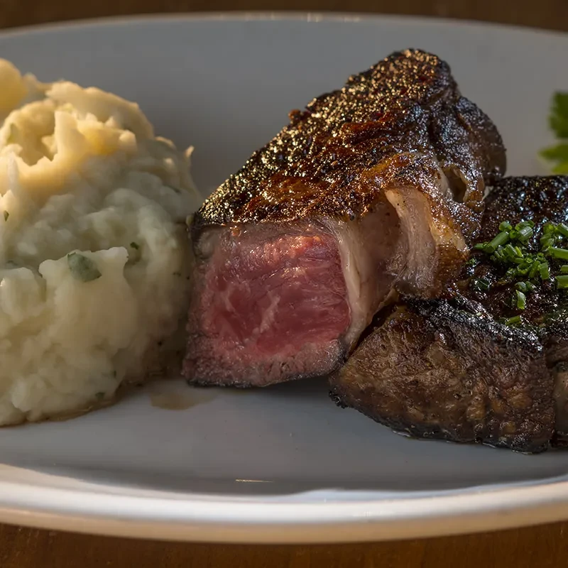 Medium-rare steak with charred crust, mashed potatoes, and green herbs.