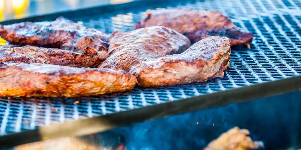 Steak cuts with char marks grilling over fire and smoke.