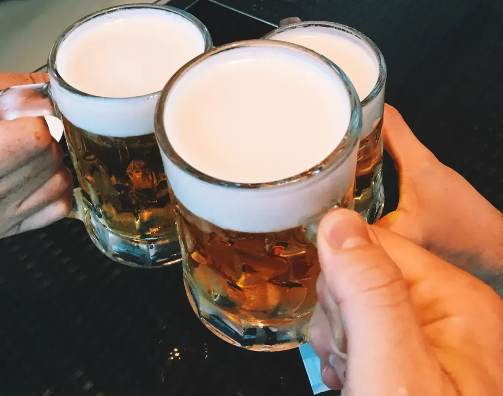Three beer mugs with foam heads, held by hands, toasting.