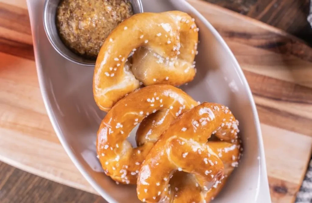 Three salted soft pretzels, whole-grain mustard, in a bowl on wood.