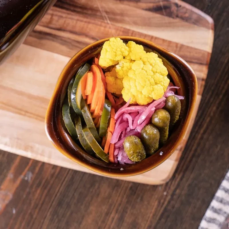 A vibrant bowl of assorted pickled vegetables on a wooden surface.