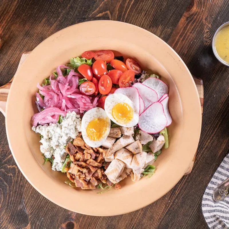 Colorful salad bowl with chicken, eggs, bacon, cheese on wooden table.