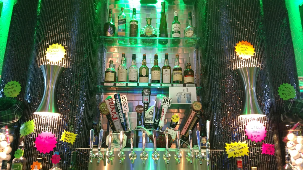 Green-lit bar with liquor bottles, beer taps, and drink special signs.