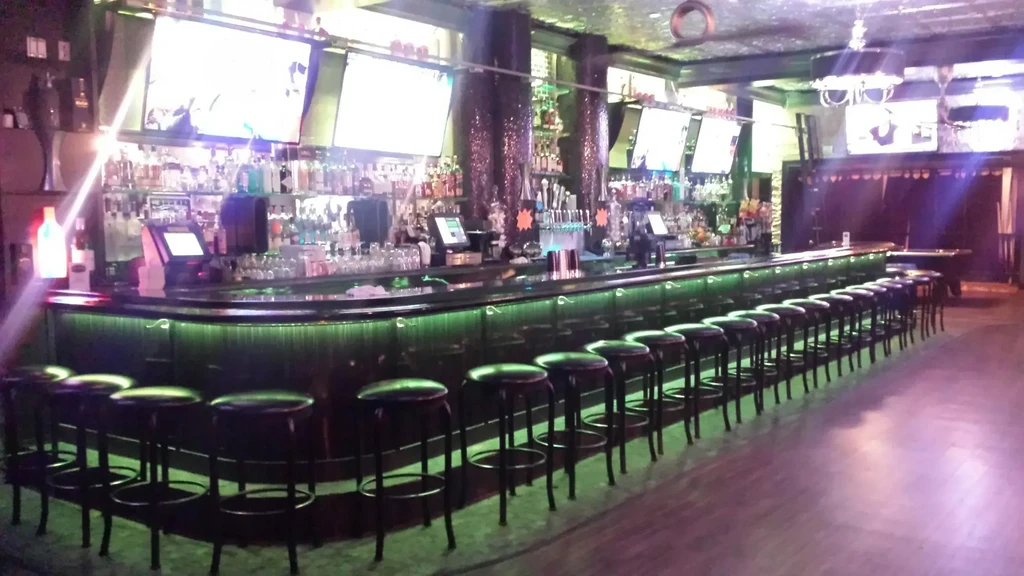 Empty, curving bar with green neon light strip, liquor shelves.