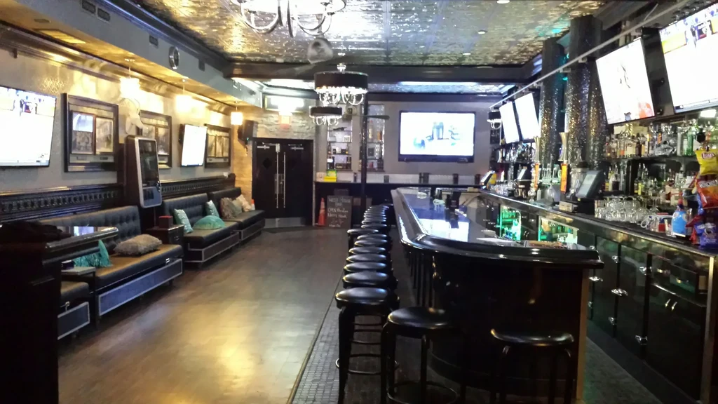 Empty, upscale bar interior with dark bar, booth seating, and TVs.