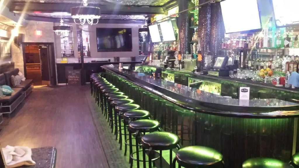 Modern bar interior with curved counter, green LED lighting, and lounge seating.