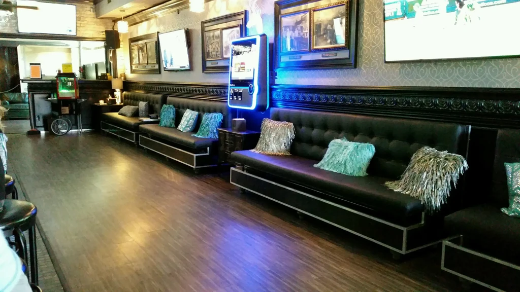 Dark lounge interior with banquette seating, artworks, TVs, and glowing jukebox.