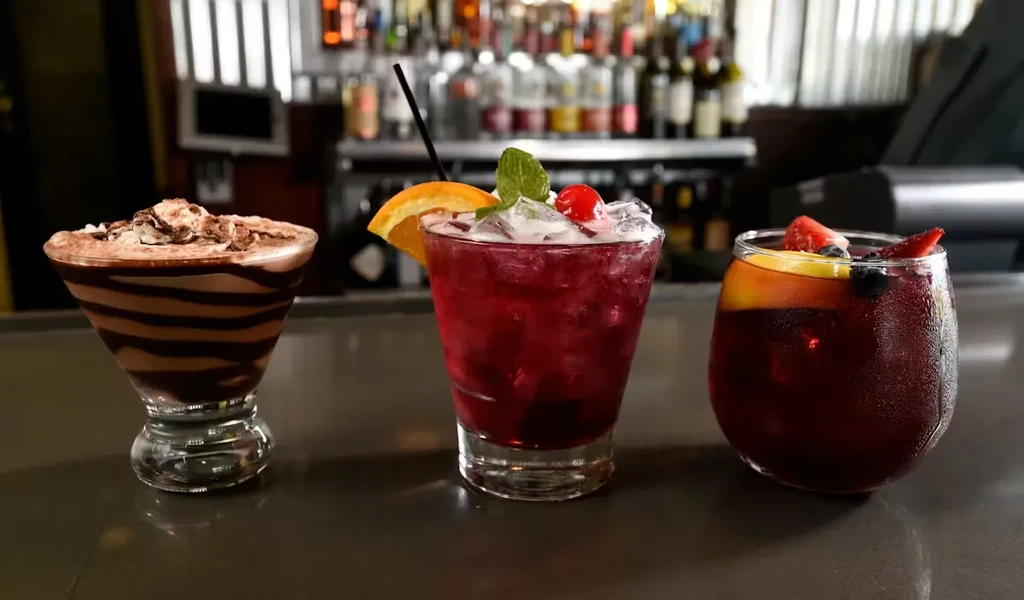 Three colorful chocolate, red cocktail, and sangria drinks on a bar.