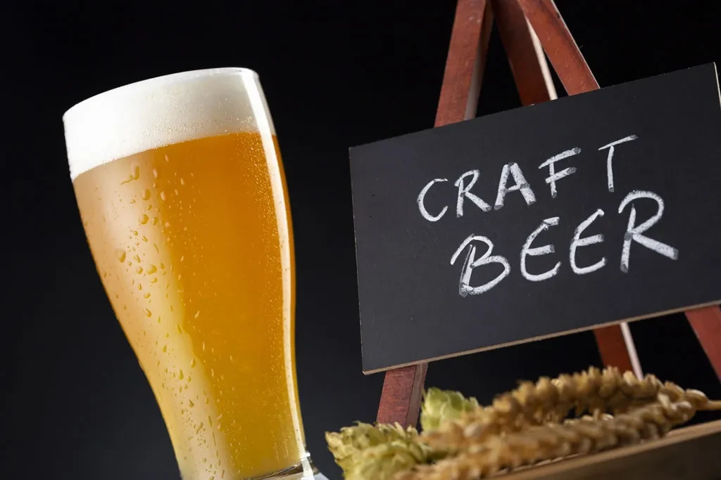 Cold craft beer, 'CRAFT BEER' sign, hops, and wheat.