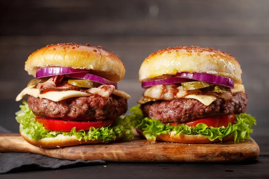 Two stacked gourmet burgers on a rustic wooden board.