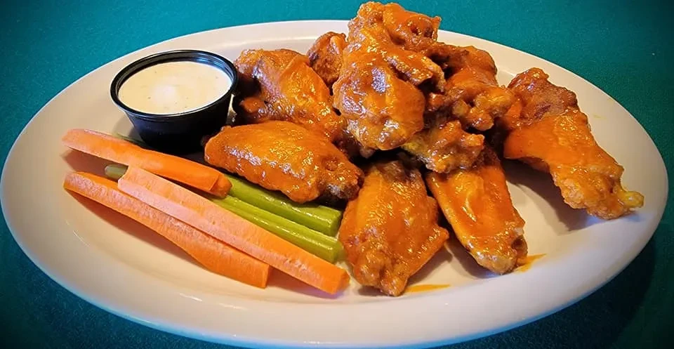 A plate of buffalo wings, carrots, celery, and dipping sauce.