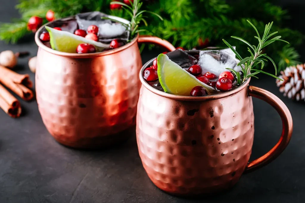 Two festive copper mug drinks with cranberries, lime, and rosemary.