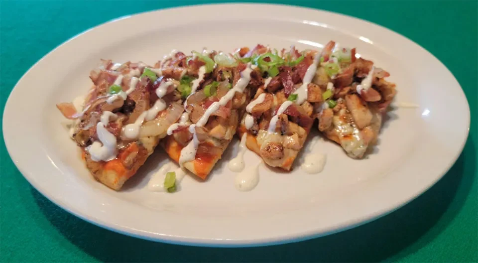 Four chicken, bacon, and onion flatbread appetizers with creamy sauce.