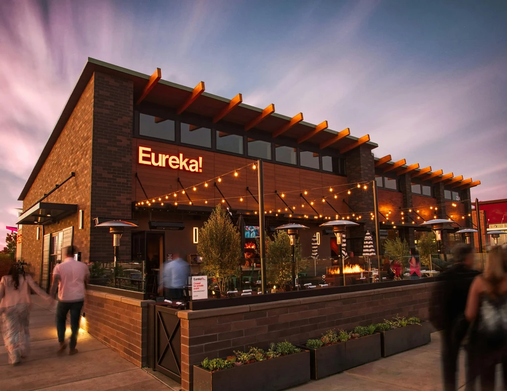 Modern Eureka! restaurant exterior at dusk with lights, heaters, and fire pit.