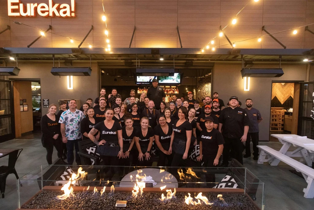 Restaurant staff posing outside Eureka! at dusk with fire pit.