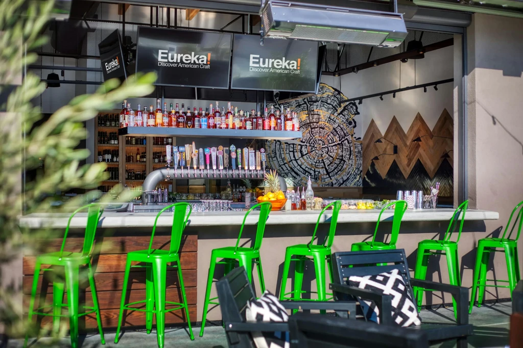 Well-stocked outdoor bar featuring beer taps, liquor, green stools, and wall art.