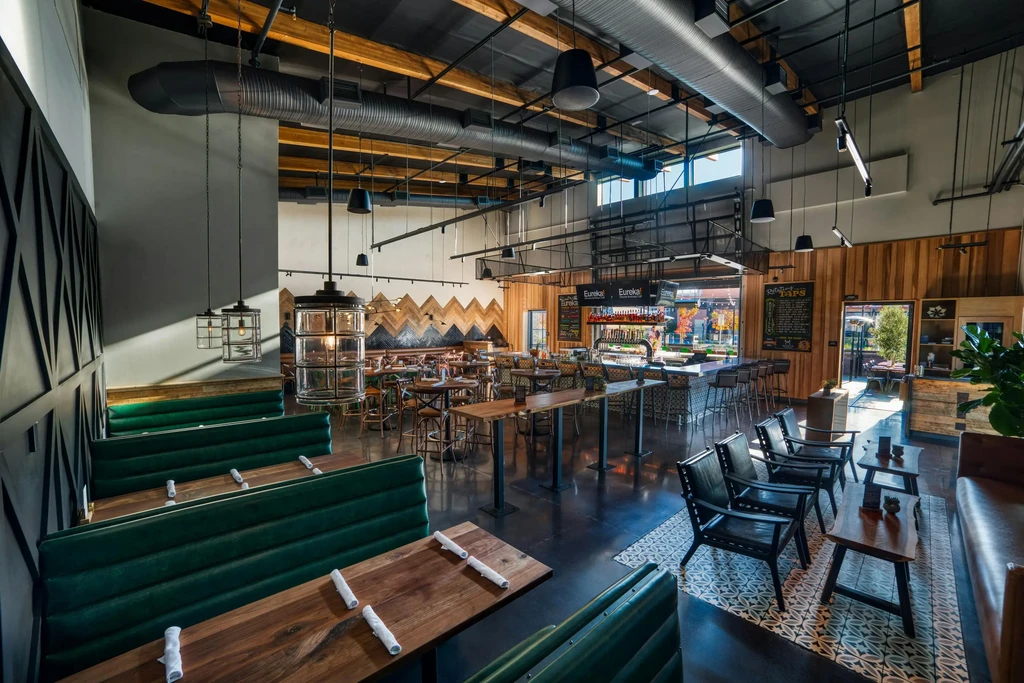 Empty, spacious modern restaurant interior with booths, bar, industrial ceiling.
