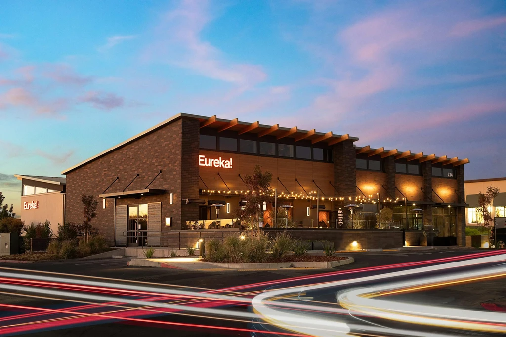 Modern "Eureka!" restaurant at dusk, patio and long-exposure car lights.