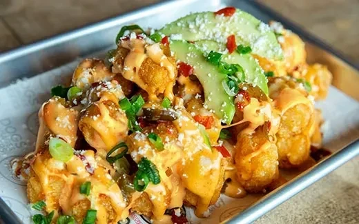 Loaded tater tots with cheese sauce, avocado, and green onions.