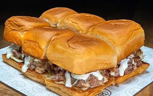 Several mini-burgers with meat, cheese, sauce on "DOG HOUSE" paper.