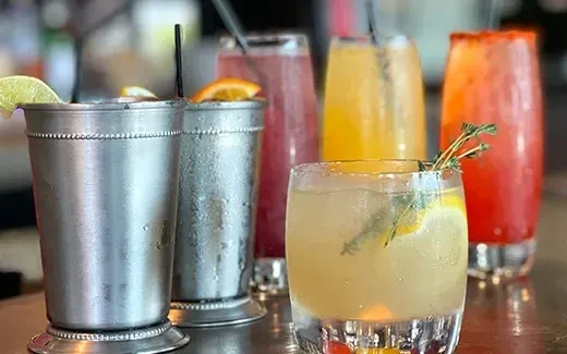 Five colorful drinks in frosted metal cups and clear glasses.