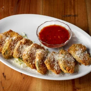 Fried food with grated cheese, lettuce, and marinara on a wood table.