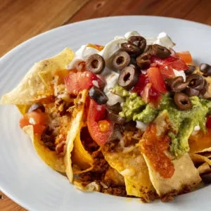 A plate of nachos with ground meat, cheese, olives, sour cream, guacamole.