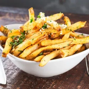White bowl overflowing with seasoned french fries on a wooden table.
