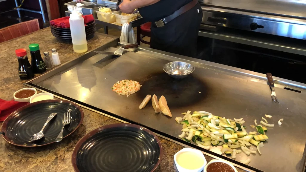 Hibachi grill cooking rice, protein, and vegetables, with a chef partially visible.