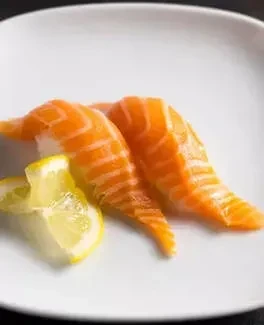Two salmon nigiri sushi pieces with lemon wedges on white plate.