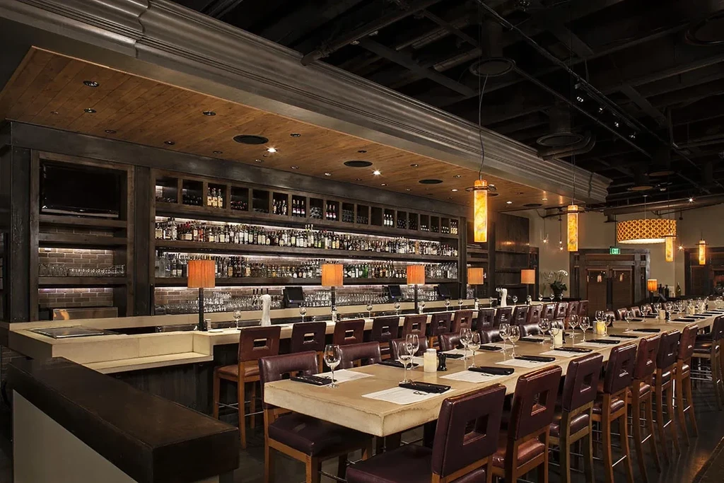 Empty upscale bar with lit liquor bottles and a long communal table.