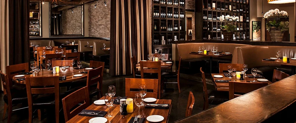 Empty, upscale restaurant interior with set tables, wine rack, and warm light.