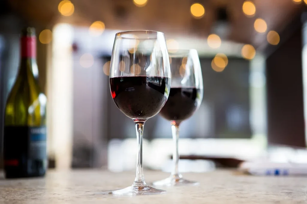 Two red wine glasses on a counter, blurred bottle and bokeh.
