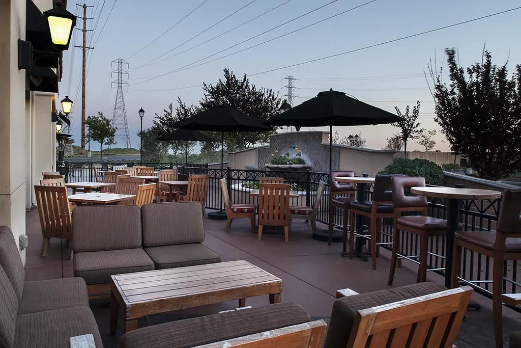 Empty outdoor restaurant patio at dusk with diverse seating and a fountain.