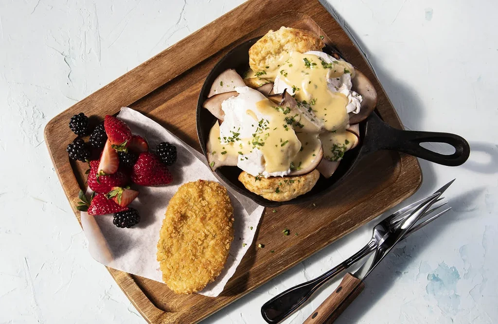 Top-down breakfast spread: Eggs Benedict skillet, fresh berries, hash brown.