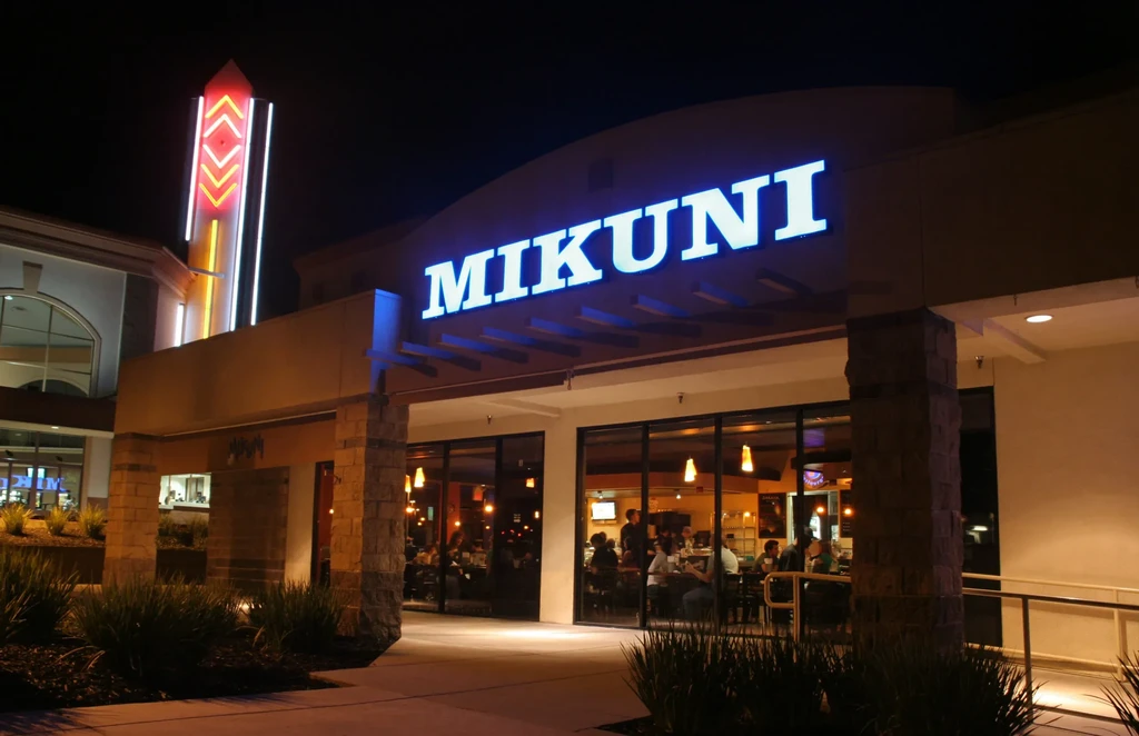 Mikuni restaurant exterior at night, blue sign, neon, diners, landscaping.