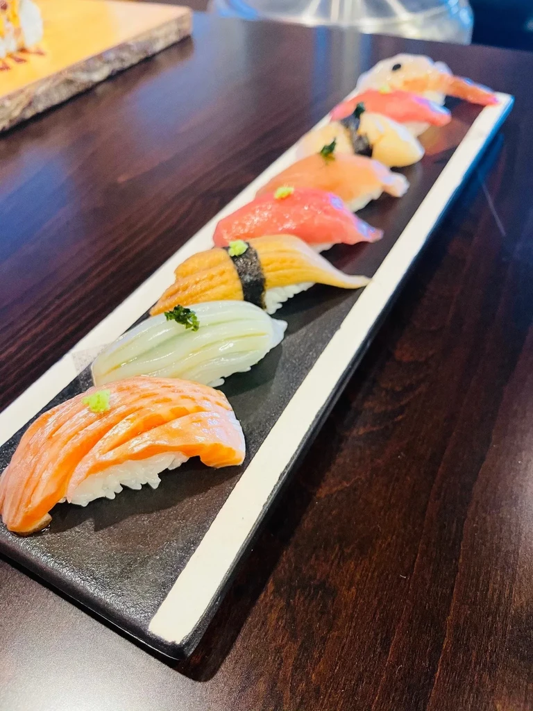 Seven assorted nigiri sushi pieces on a black and white serving dish.