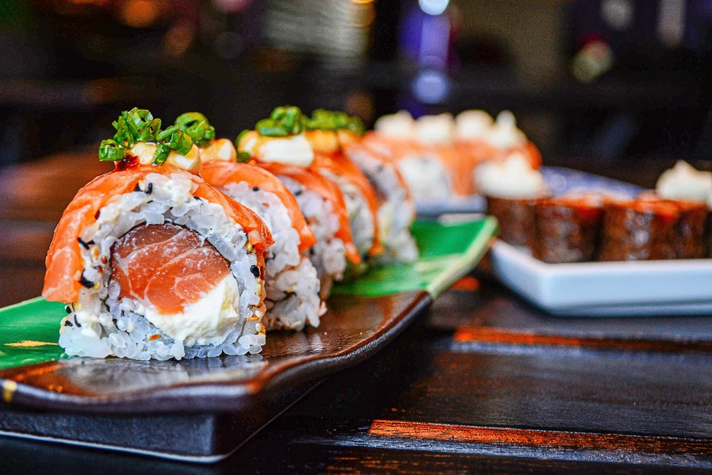 Salmon maki sushi rolls with cream cheese and chives on a dark plate.