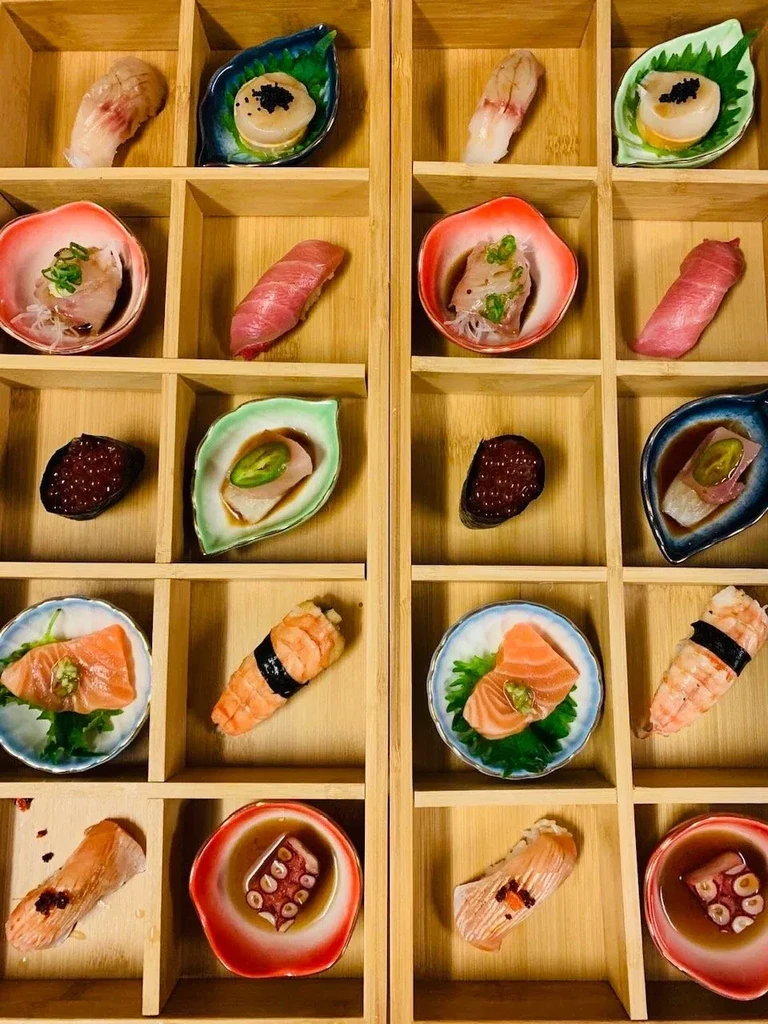 Meticulously arranged sushi, sashimi, and appetizers in a 24-compartment bento box.