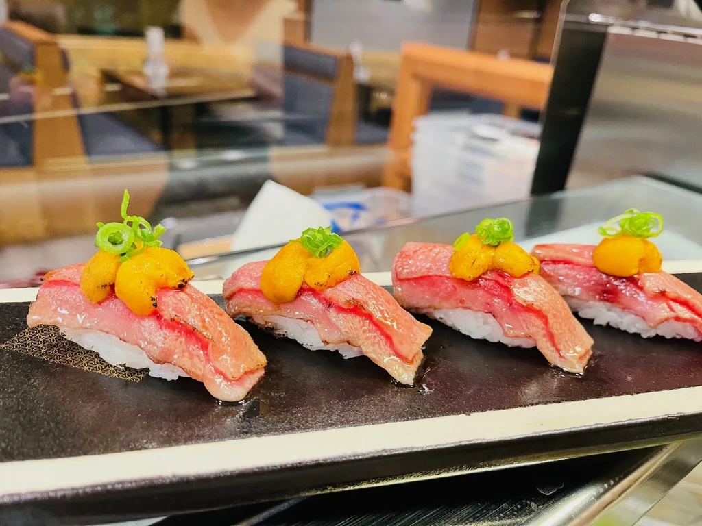 Four beef and uni nigiri with green onions on a dark plate.