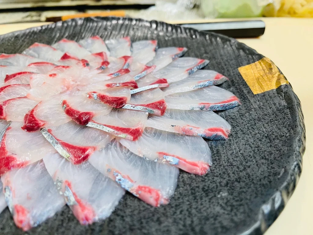 White fish sashimi arranged in a floral pattern on a dark textured plate.