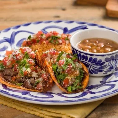 Three meat tacos, rice, pinto beans on a blue-patterned Talavera plate.