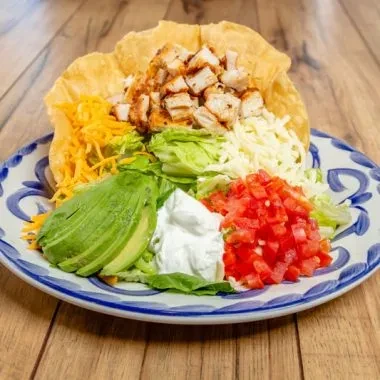 Crispy tortilla bowl taco salad with chicken, cheese, avocado, and tomatoes.