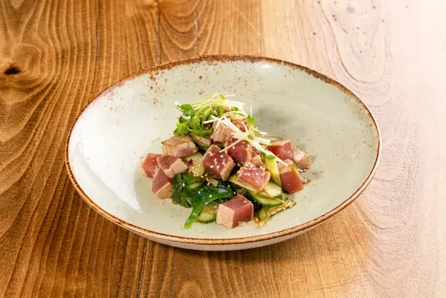 Rare tuna poke with greens on a rustic wooden table.