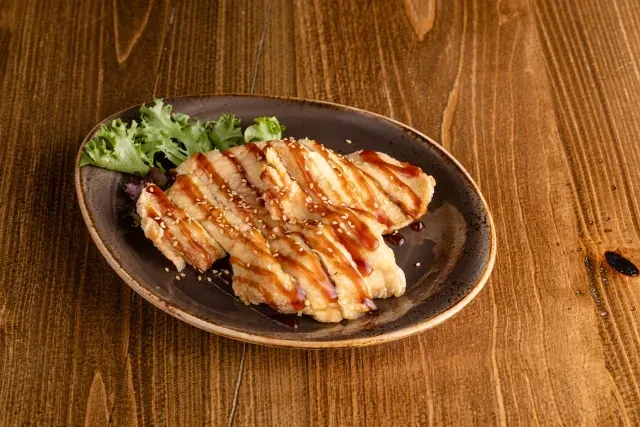 Oval plate with sliced, pan-fried food, dark sauce, sesame, lettuce.