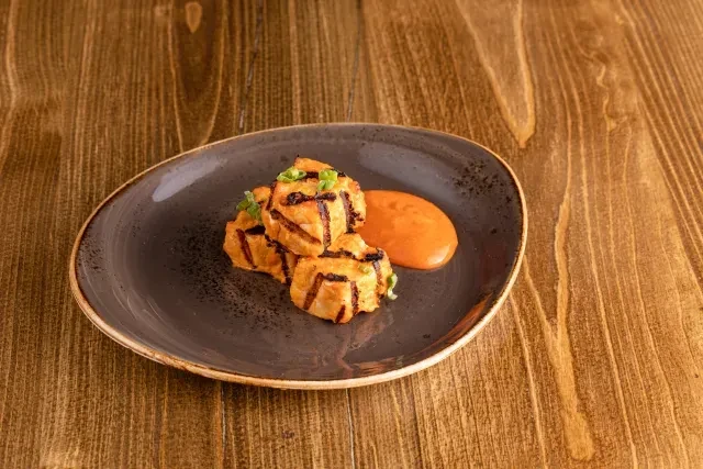 Grilled food with crosshatch marks, herbs, and sauce on a dark plate.