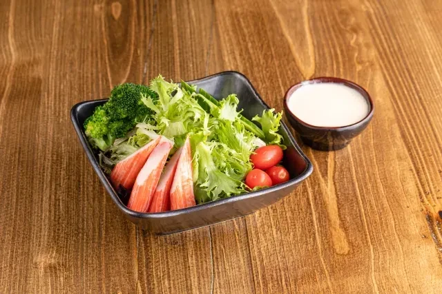 Salad with lettuce, broccoli, tomatoes, crab sticks, and dressing.